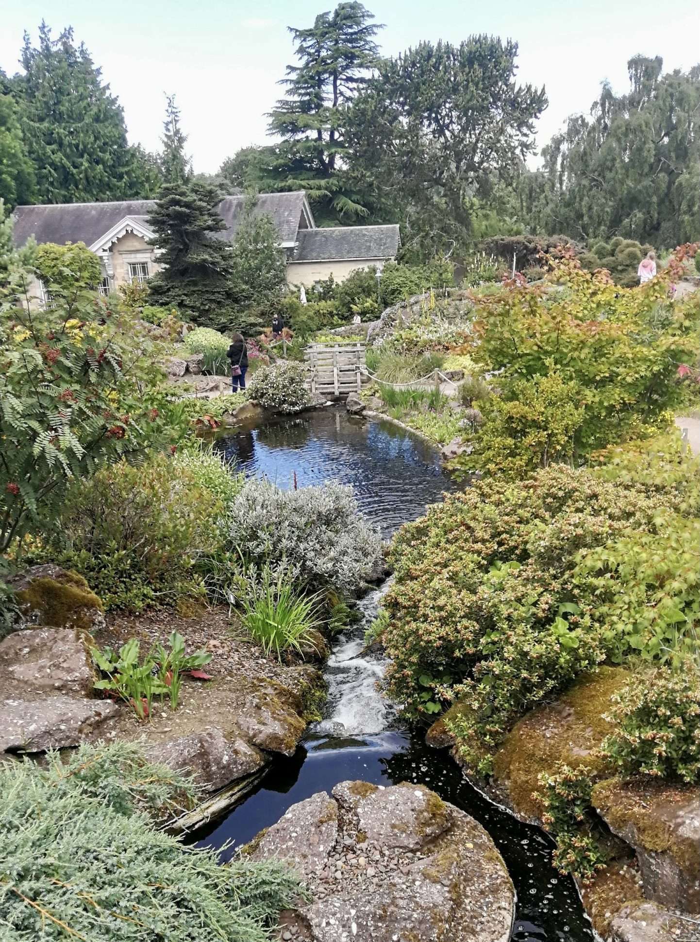 Cascata finisce in un lago attorno al verde e rocce e sullo sfondo una casetta