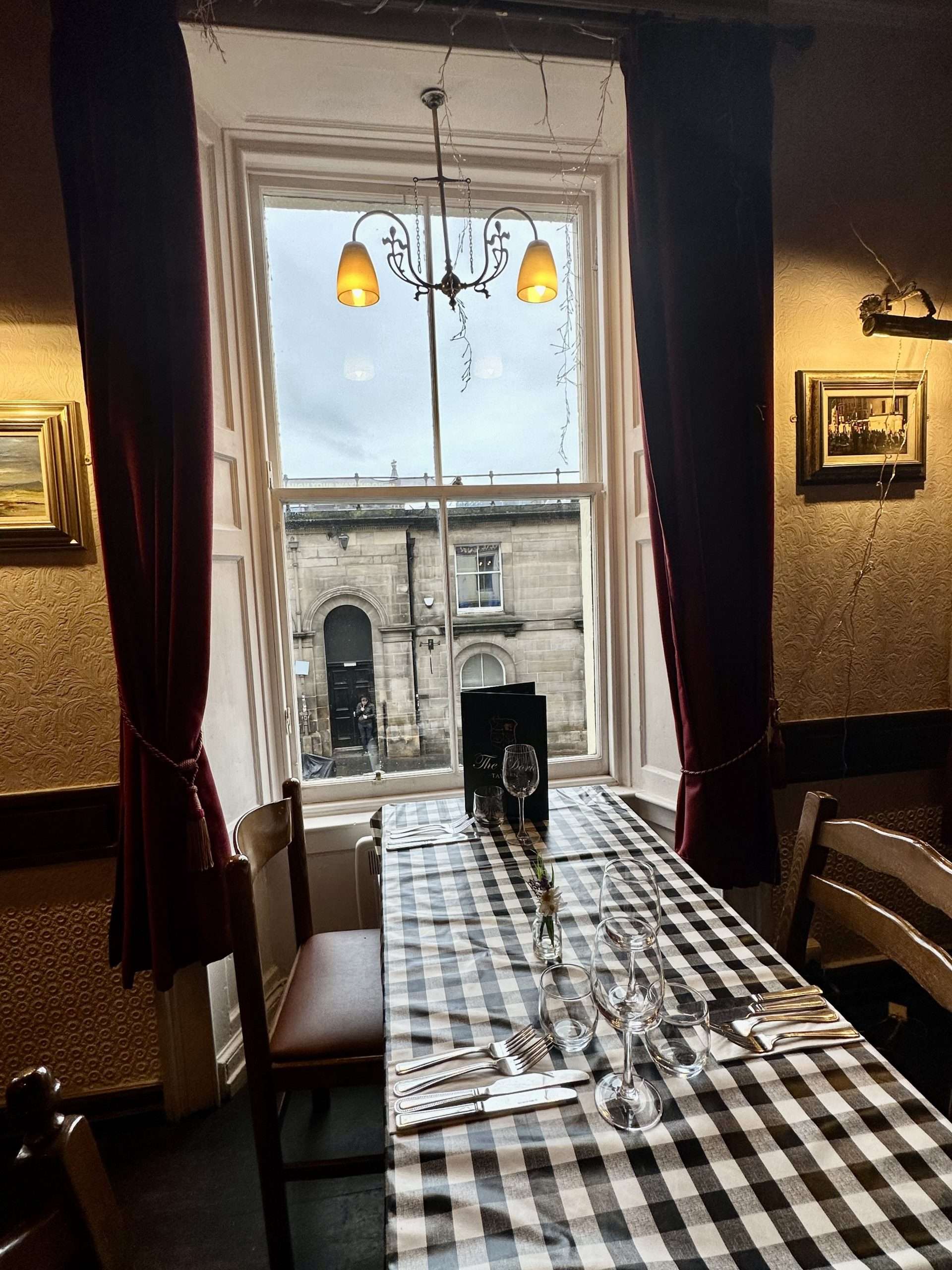 Tavolo con tovaglia a scacchi bianco e nera, sedie di legno, davanti a finestra con tendoni rossi