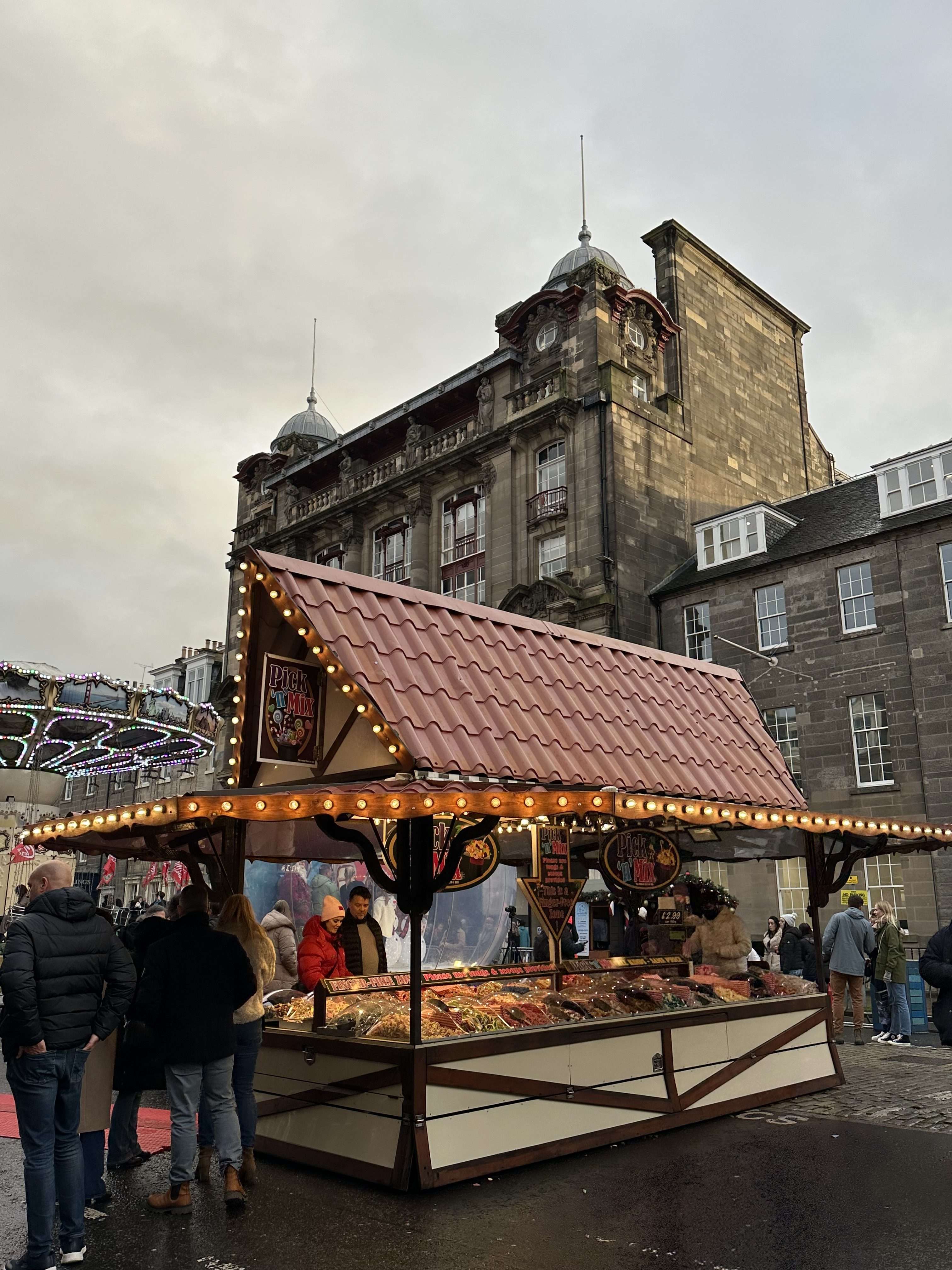 Casetta mercatini di Natale con bancarelle e scorcio di giostra illuminata