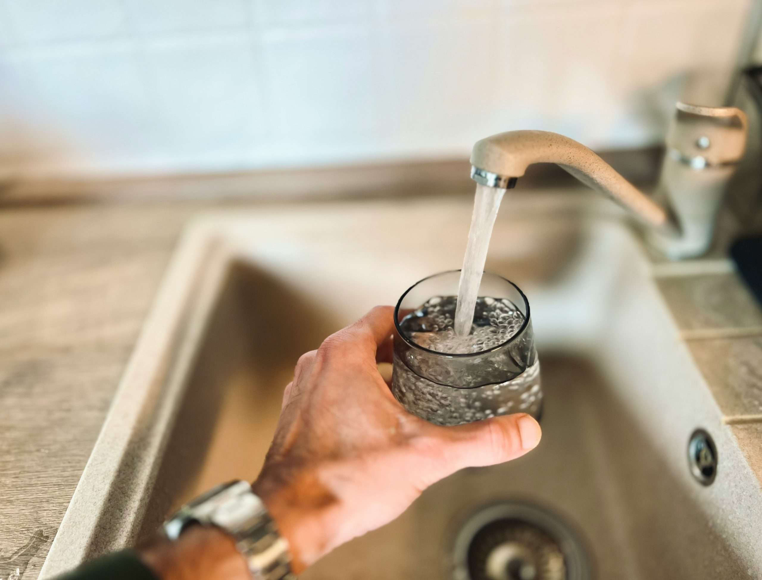 Acqua che esce dal rubinetto lavandino e riempie bicchiere tenuto da una mano