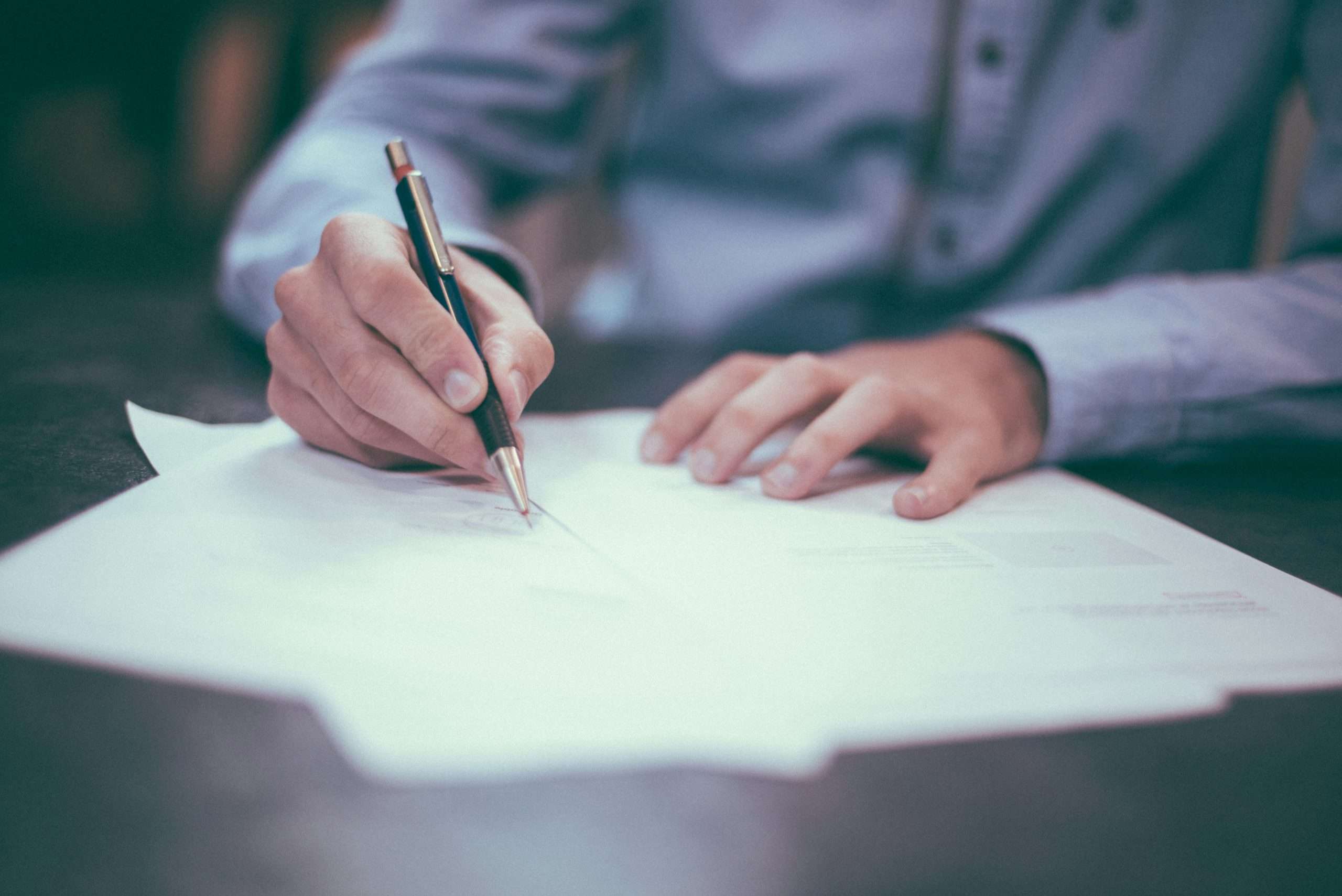 Mani di uomo che scrive su fogli sparsi su un tavolo di legno per prepararsi a un colloqui per lavoro in UK