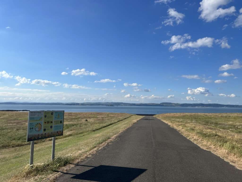 Strada asfaltata con prato verde ai lati e dritto il mare di Edimburgo