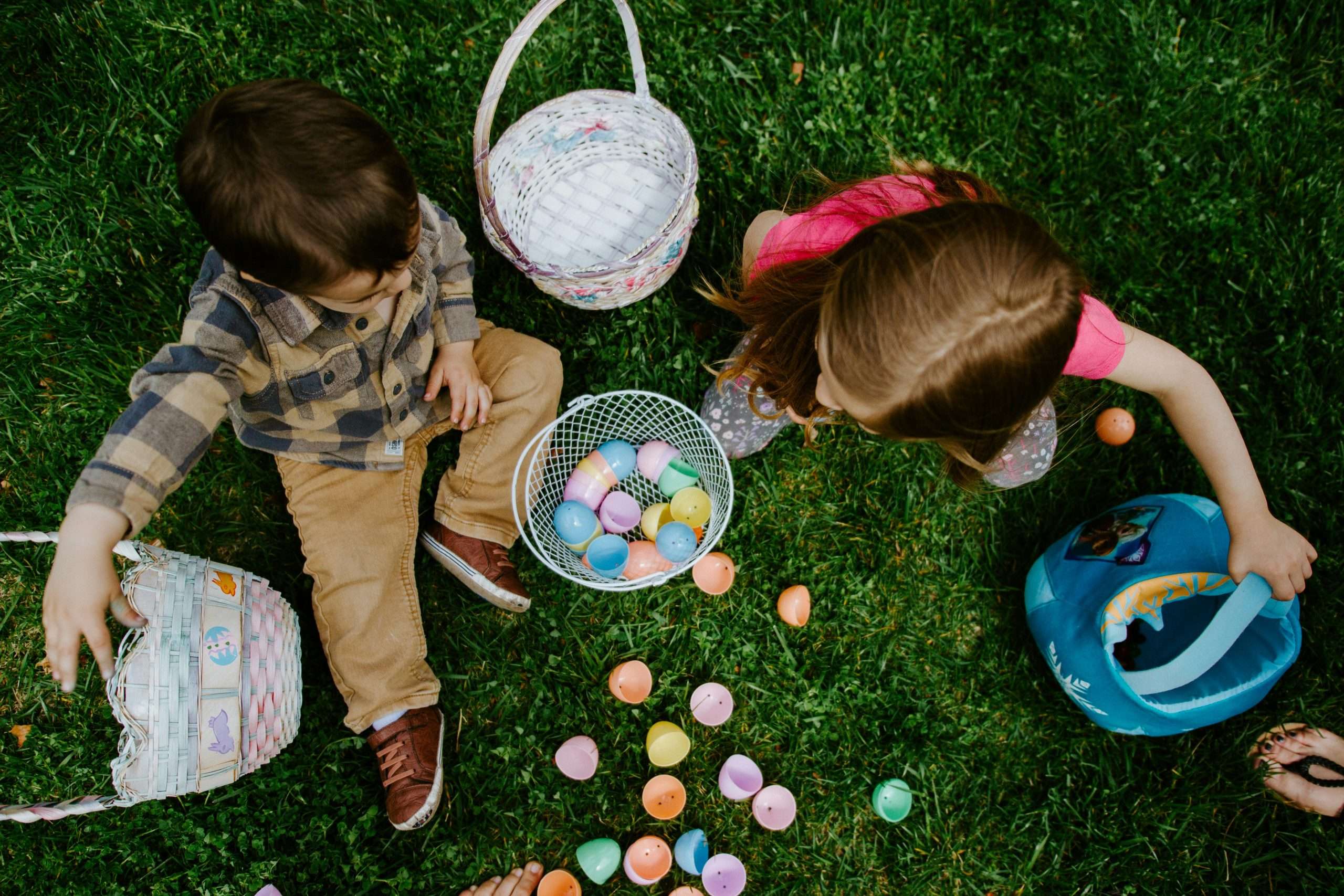 due bambini seduti sul prato con un cesto di uova di pasqua