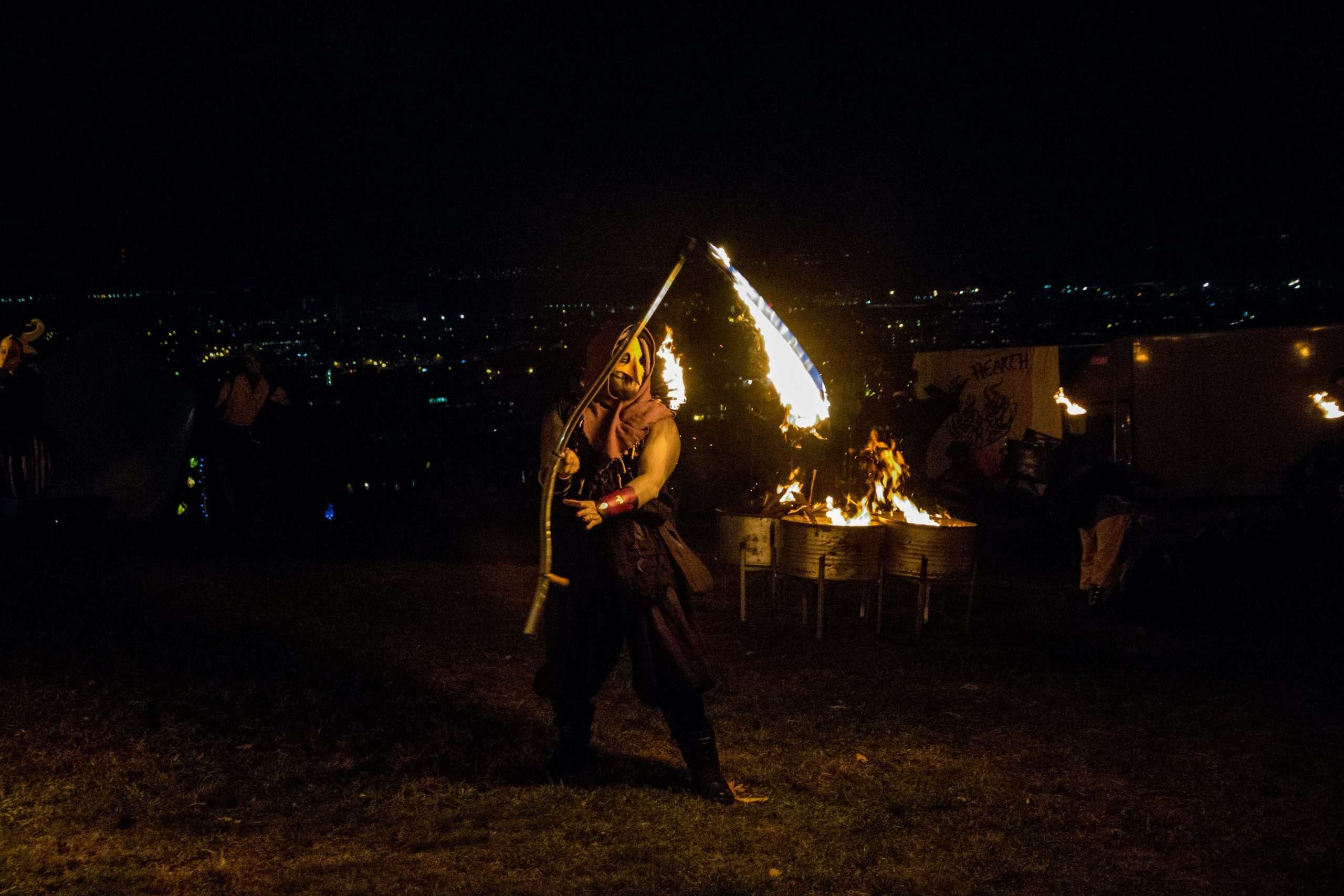 Persona con maschera e fiaccola in mano che gira attorno a un falò mentre altra gente balla di notte al Beltane fire festival di Edimburgo