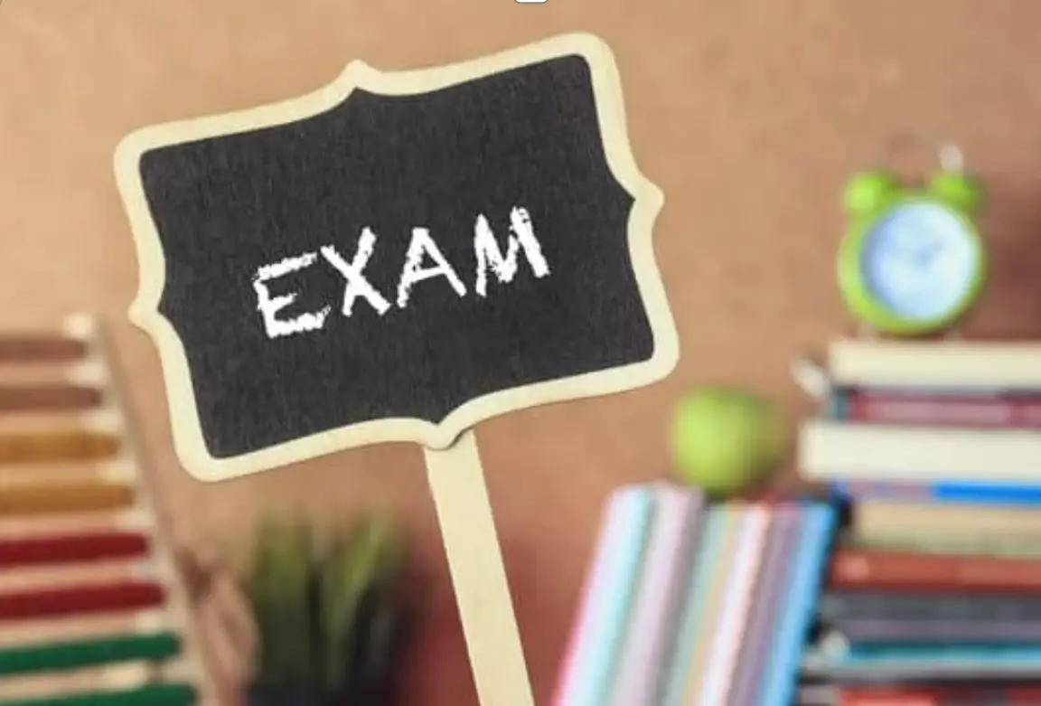 scritta 'EXAM' su una lavagnetta con libri sullo sfondo