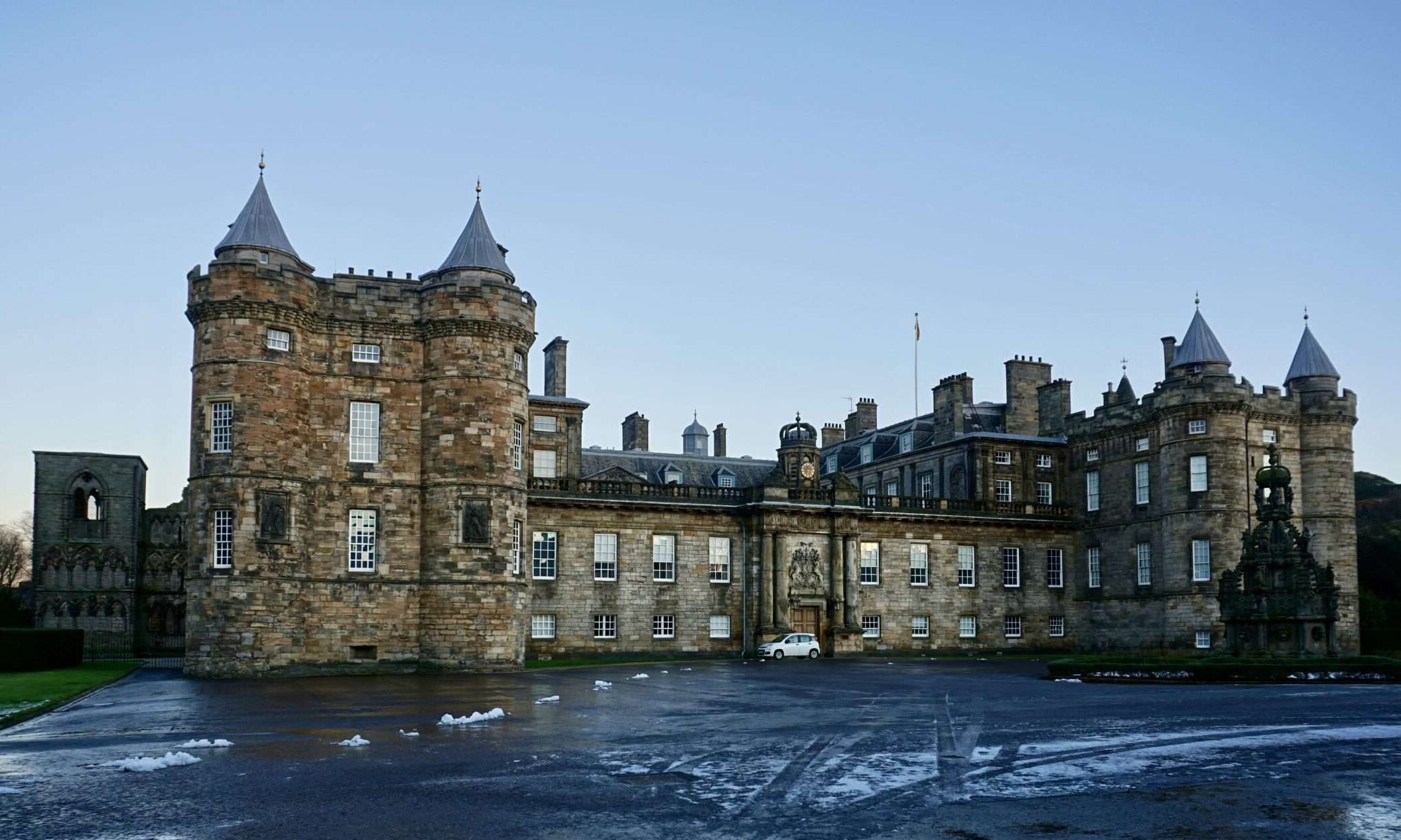 Facciata esterna del Palace of Holyroodhouse a Edimburgo con la torre storica di Maria Stuarda e i resti dell'abbazia sotto un cielo limpido.