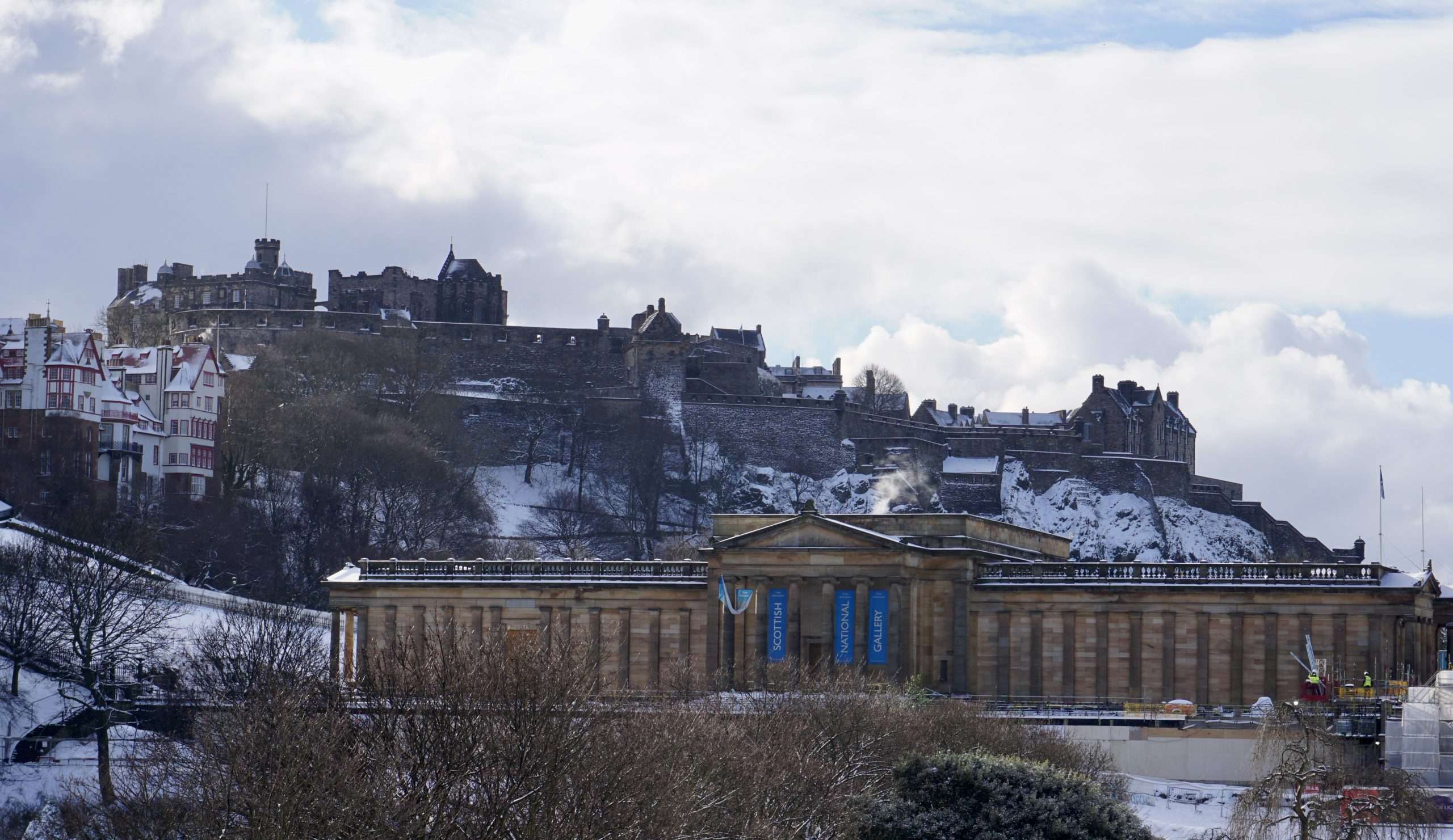La Scottish National Gallery di Edimburgo coperta di neve con l'imponente Castello di Edimburgo che svetta sullo sfondo sotto un cielo invernale.