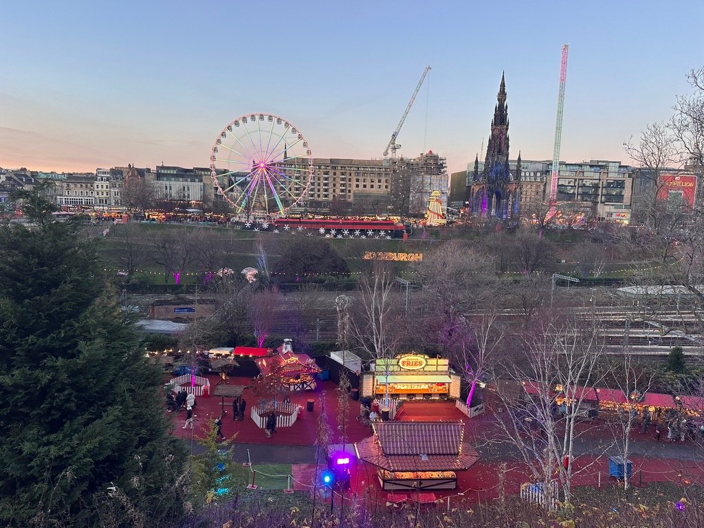 Illustrazione dei mercatini di Natale a Edimburgo con il castello sullo sfondo, la ruota panoramica e la giostra Starflyer.
